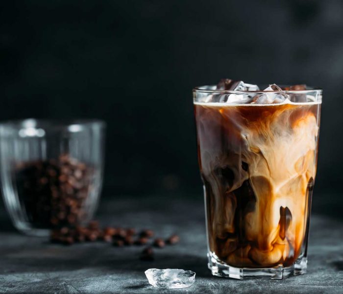milk-being-poured-into-iced-coffee-on-a-dark-table-TH2MABV.jpg